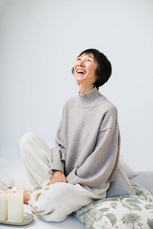 chinese-woman-wellness-coach-laughing-on-cushion-with-candles-by-london-professional-photographer