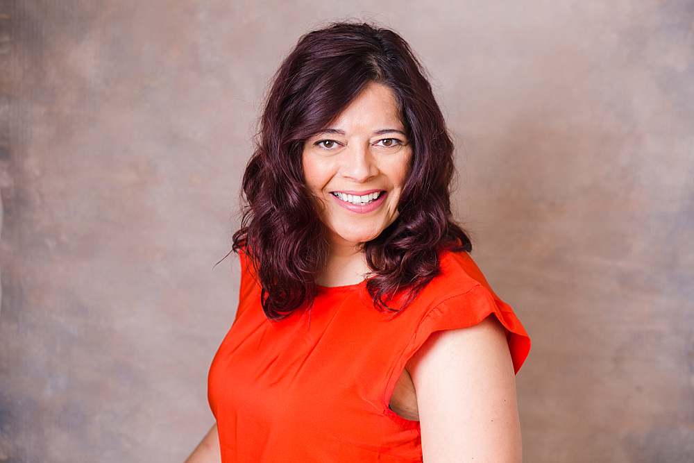 linkedin-photo-of-middle-age-woman-in-orange-top-smiling-in-front-of-pink-background-by-london-linkedin-headshot-phographer