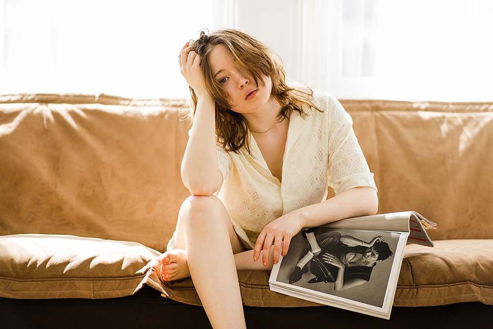 editorial-portrait-girl-reading-magazine-cross-leg-sitting-on-sofa-head-resting-on-hand