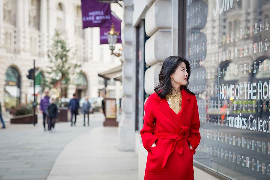 Stylish woman in a red coat walking by a reflective shop window on a London high street