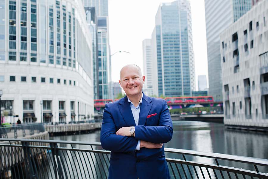Businessman in a blue suit standing in front of modern office buildings and a canal at Canary Wharf