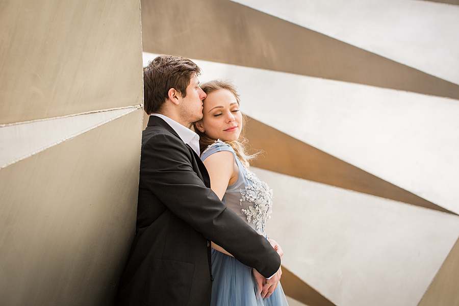 Couple in elegant attire embracing in front of a modern architectural wall in the City of London